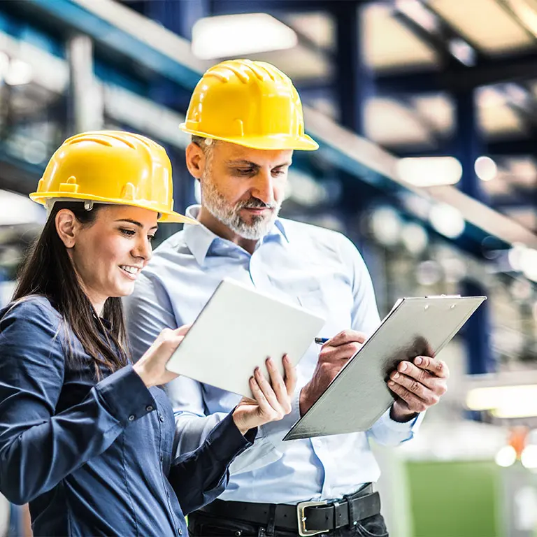 workers in hard hats looking at a tablet and clip board