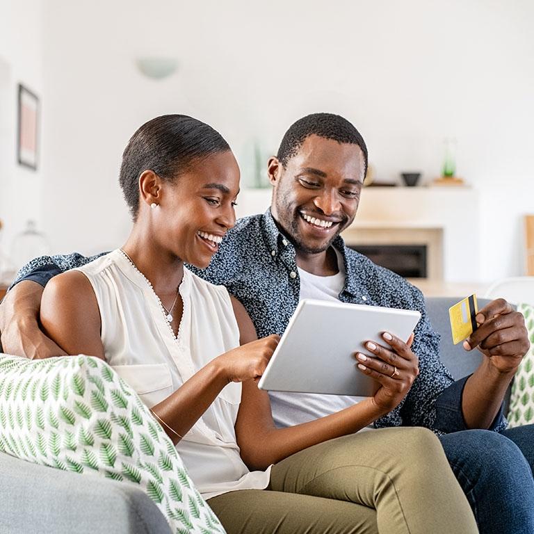a couple sitting in a couch interacting with a tablet and using a credit card