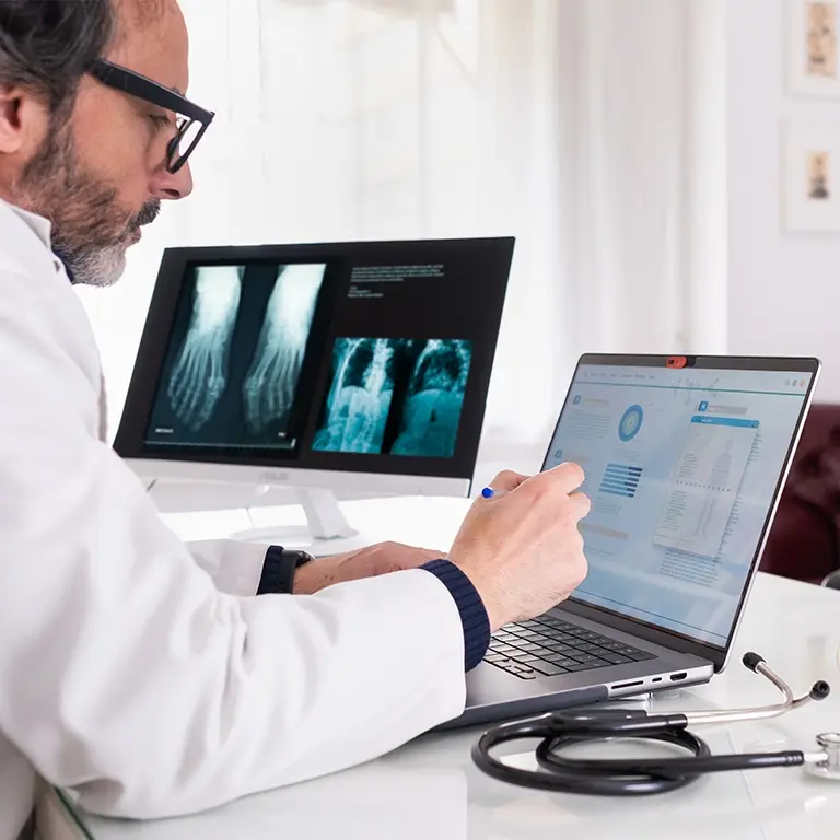 doctor looking at laptop and monitor with health records