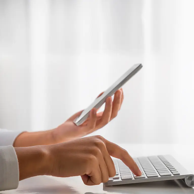 hands holding smartphone and touching a laptop keyboard