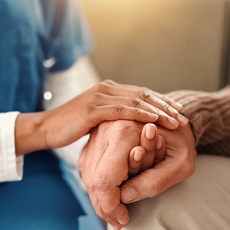 Close up view of a home healthcare nurse holding the hand of their patient
