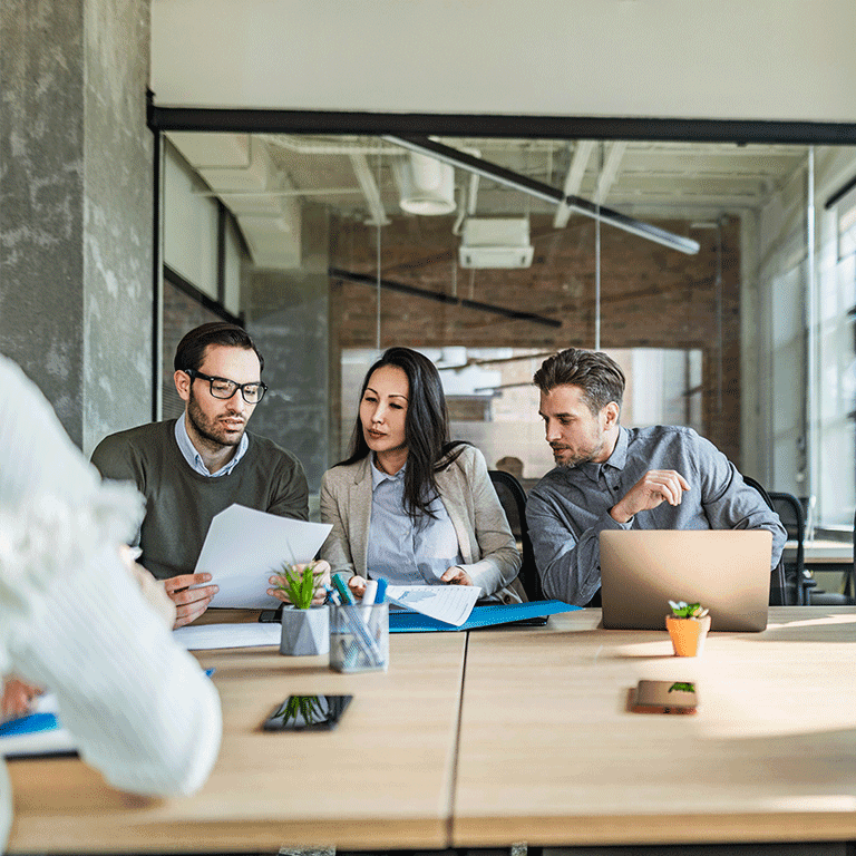 co workers gathered around a laptop looking at paper reports