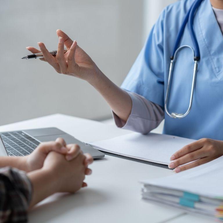 healthcare worker in scrubs at desk talking to another person