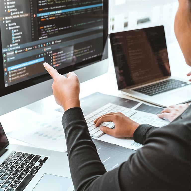 person pointing to a computer screen with code programs open in an office setting