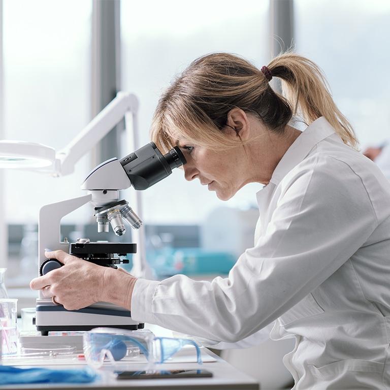 person in lab coat looking into microscope