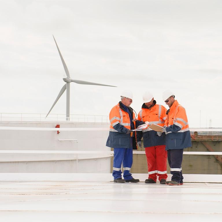 people in reflective gear standing in front of a wind turbine