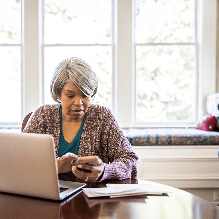 woman on phone behind laptop in bright room