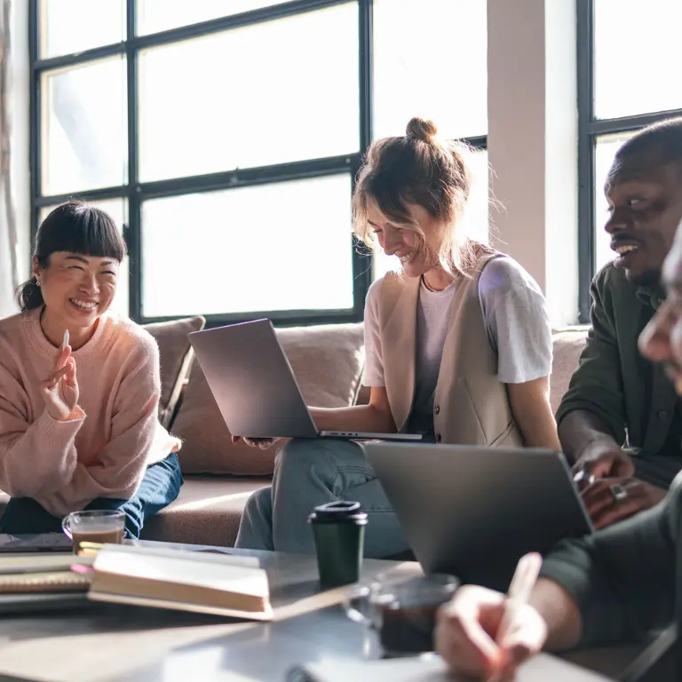 people sitting around a coffee table with laptops, laughing