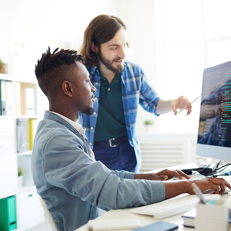 in an office setting two co-workers looking to a monitor screen with code